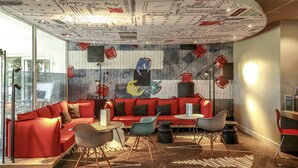 A modern lounge with a curved ceiling, red seating, and a mural with abstract figures. - ibis Orange Sud (Orange)