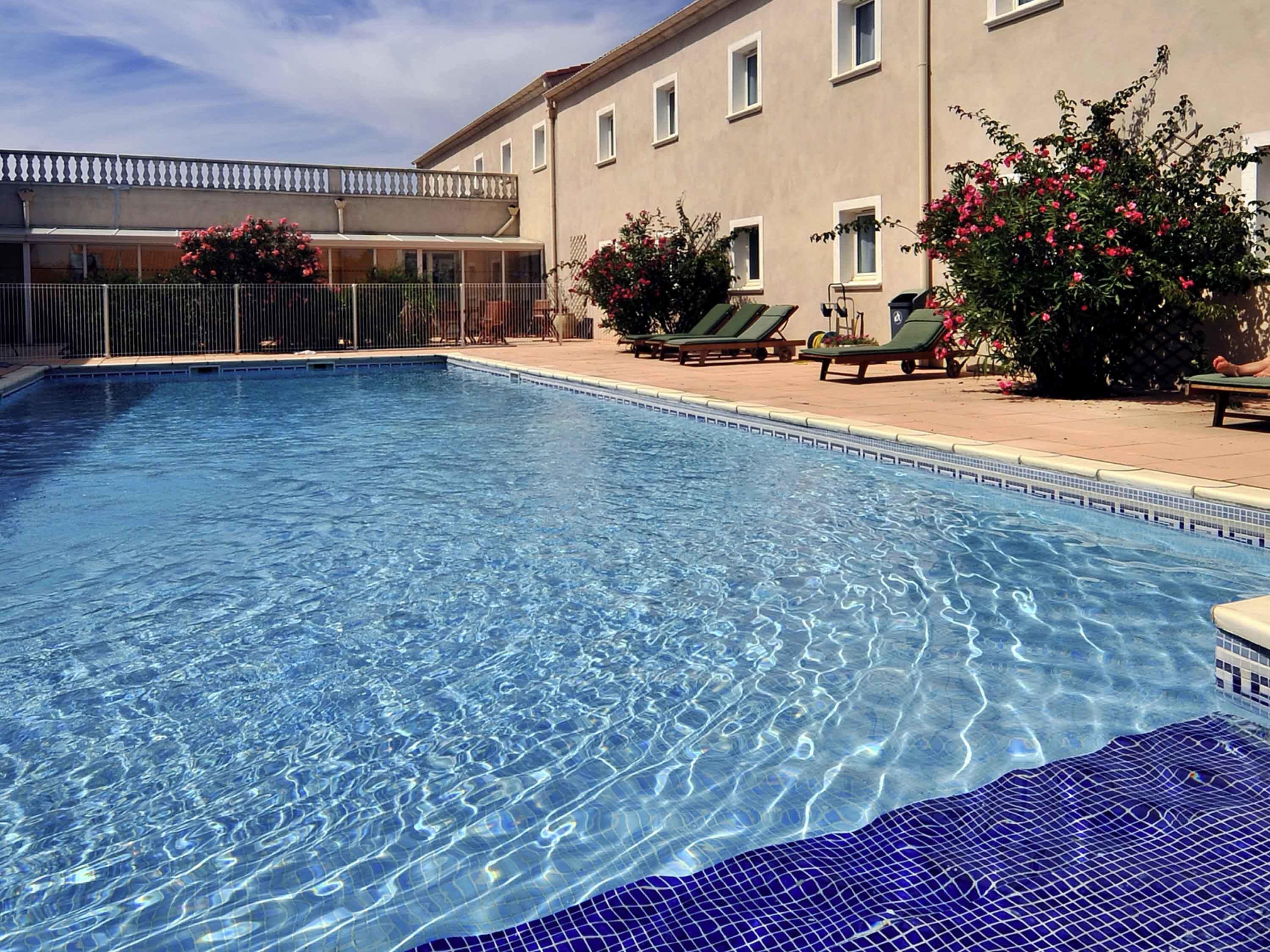 A clear swimming pool with lounge chairs and a building in the background.