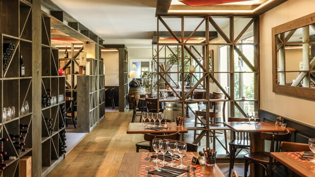 A restaurant interior with wooden tables, chairs, and a wine rack. - ibis Orange Sud (Orange)