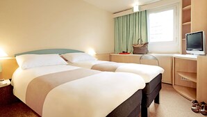 A hotel room with two beds, a desk with a computer, a window with curtains, and a pair of shoes on the floor. - ibis Leiria Fatima (Leiria)