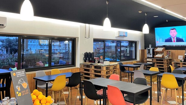 A restaurant with multiple tables and chairs, a television screen, and a view of the outside through large windows. - ibis Leiria Fatima (Leiria)