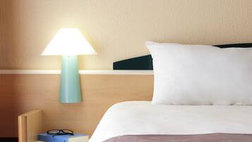 A neatly made bed with white bedding and a teal bedside lamp.