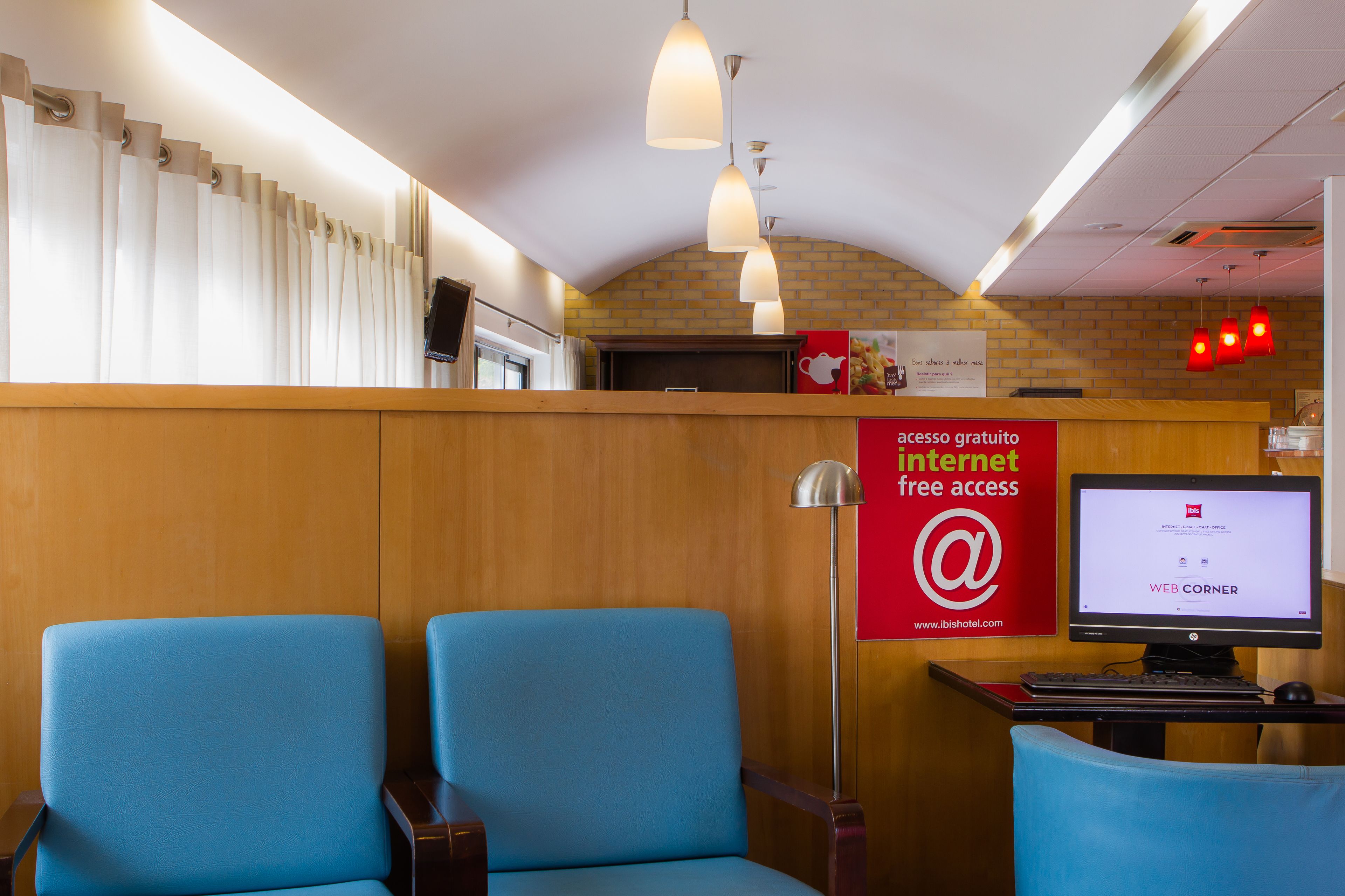 Un'area reception con un bancone in legno, due sedie blu, un monitor per computer e un cartello che offre accesso a internet gratuito.