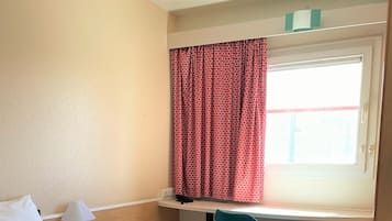 Ein Hotelzimmer mit Bett, Schreibtisch, Stuhl und einem Fenster mit Vorhängen.