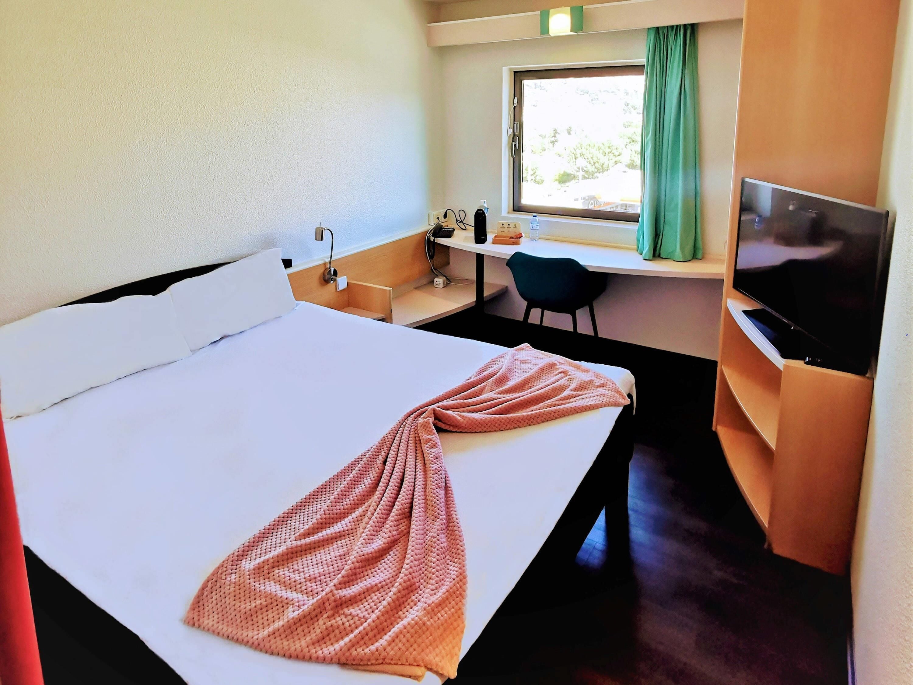A hotel room with a bed, a desk, a chair, a television, and a window with curtains.
