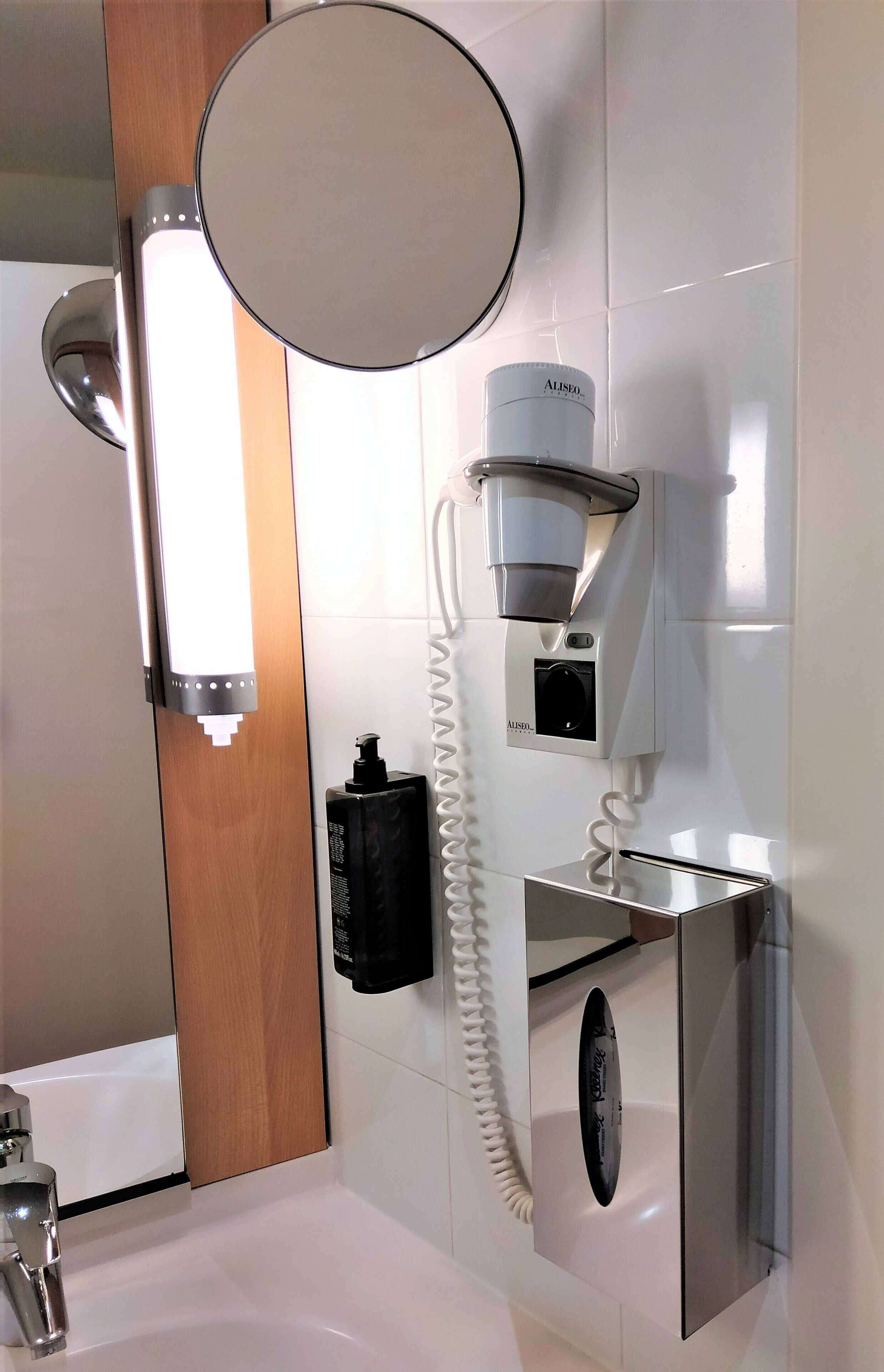 Un baño moderno con inodoro integrado, espejo, cafetera y secador de manos.