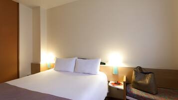 A hotel room with a large bed, bedside lamps, a nightstand, and a chair with a bag.