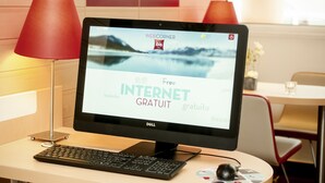 A computer monitor displaying a hotel website with "Free Internet" text, a keyboard, a mouse, and a red lamp on a desk. - ibis Leiria Fatima (Leiria)