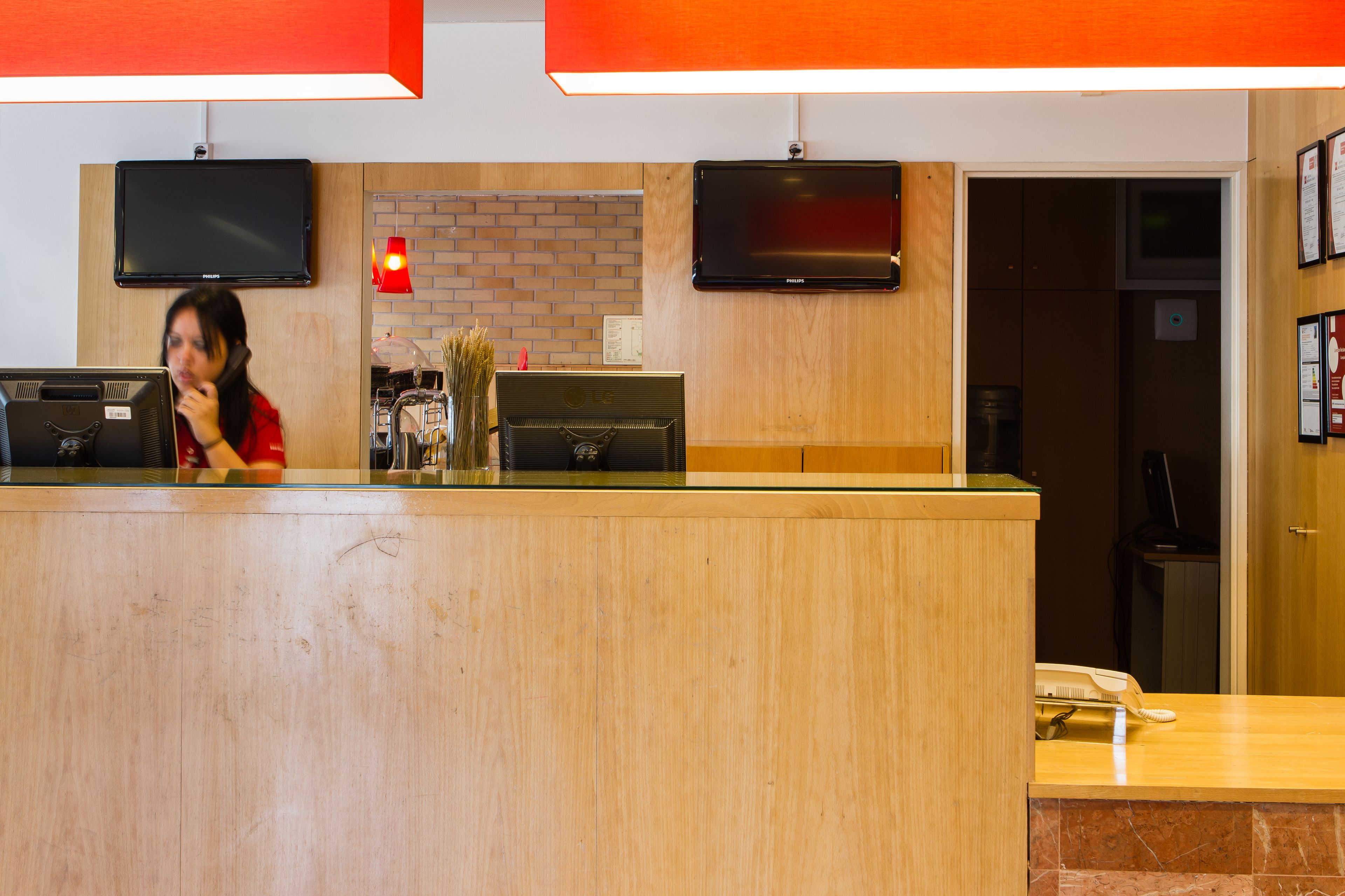 A reception desk with a flat-screen TV, a telephone, and a vase with dried plants.