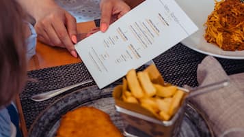 A menu with food items and prices, a plate with spaghetti, a breaded cutlet, and a container of fries.