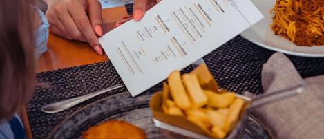 Un menú con opciones de comida y precios, un plato de espagueti, una milanesa y un recipiente con papas fritas.