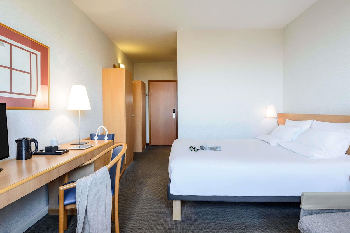 A hotel room with a bed, desk, chair, and a television.
