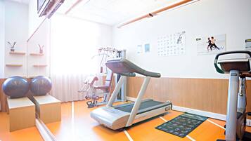Un gimnasio con equipamiento de ejercicio, una cinta de correr y una pared decorada con carteles de fitness.