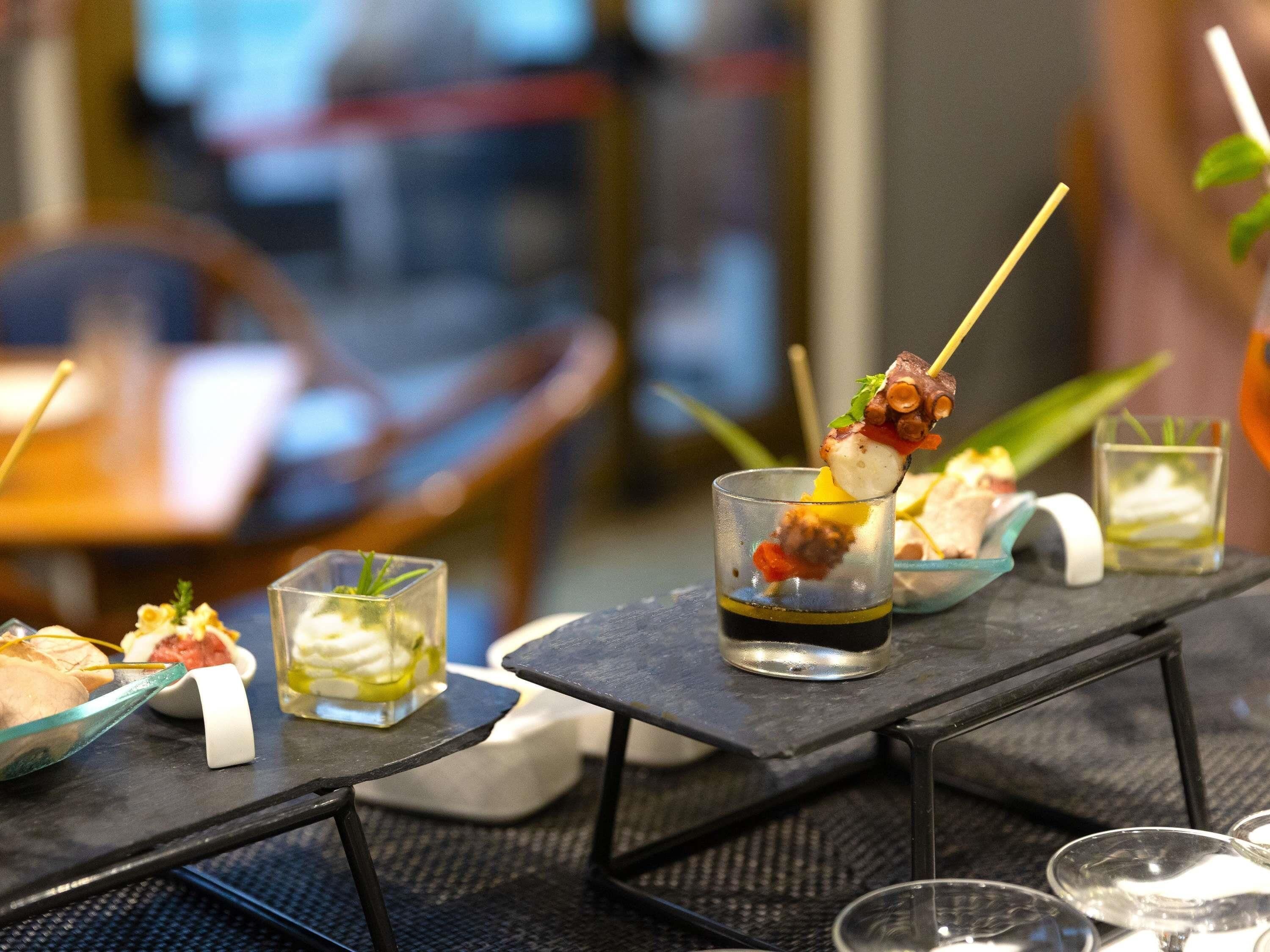 A dining setup with a glass of dark liquid, skewered food, and small dishes on a table.