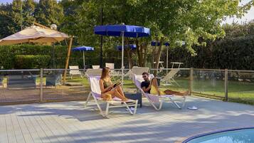 Zona junto a la piscina con sillones de descanso, sombrillas y una alberca.