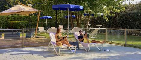 Zona junto a la piscina con sillones de descanso, sombrillas y una alberca.