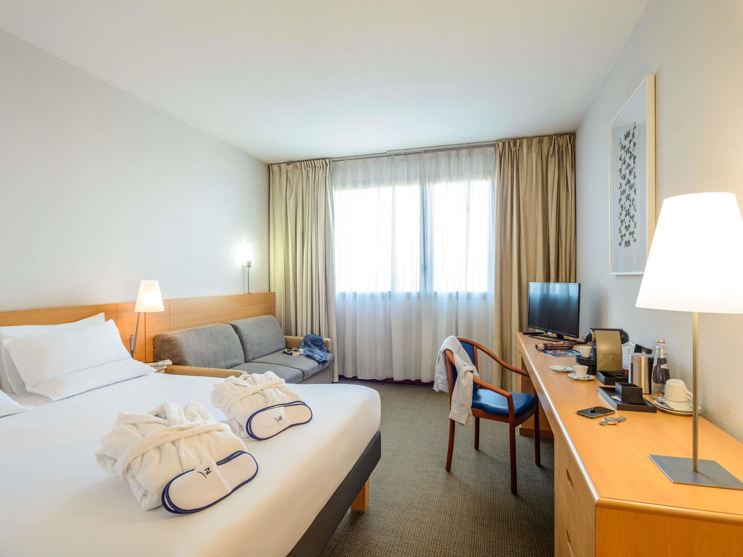 Una habitación de hotel con cama, sofá, escritorio con televisor y una silla.