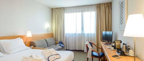 Una habitación de hotel con cama, sofá, escritorio con televisor y una silla.
