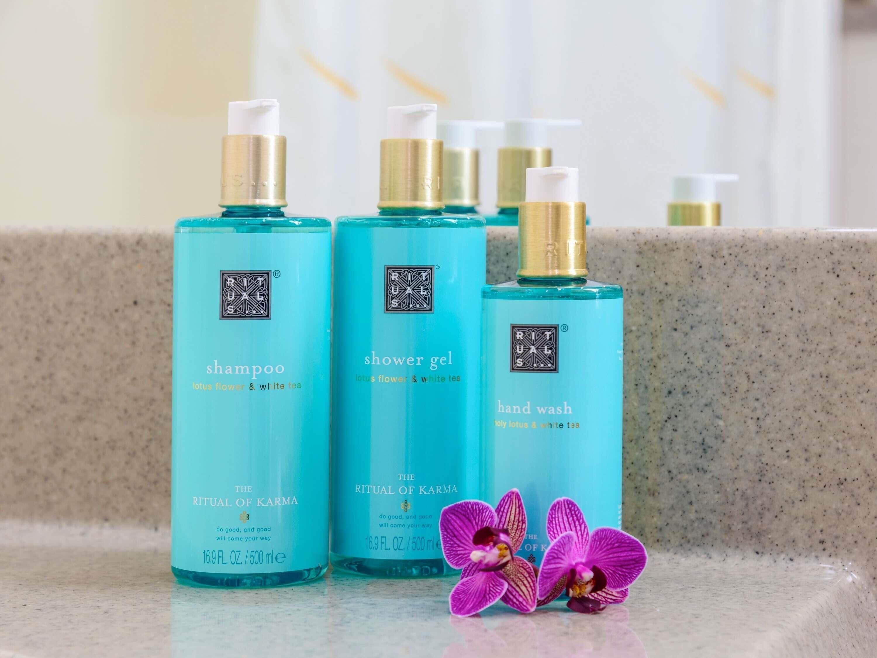 Three bottles of The Ritual of Karma products on a countertop with a marble surface.