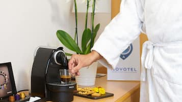 Una persona con bata preparando una bebida con una máquina de café Krups, una foto enmarcada y una bandeja de galletas sobre una encimera de madera.