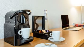 Uma cafeteira, duas chávenas, uma colher e um laptop sobre uma mesa de madeira.