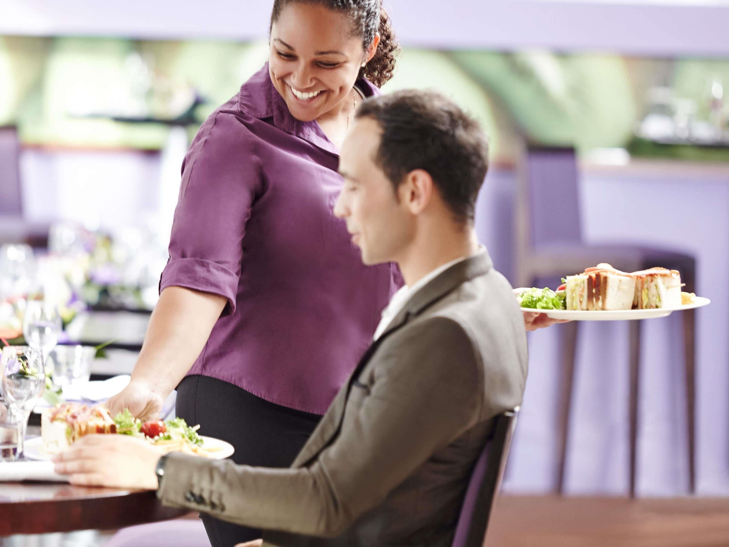 A dining table with a person serving food to another seated individual.