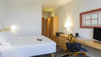 Habitación de hotel con cama, escritorio, silla, lámpara, televisor y armario.