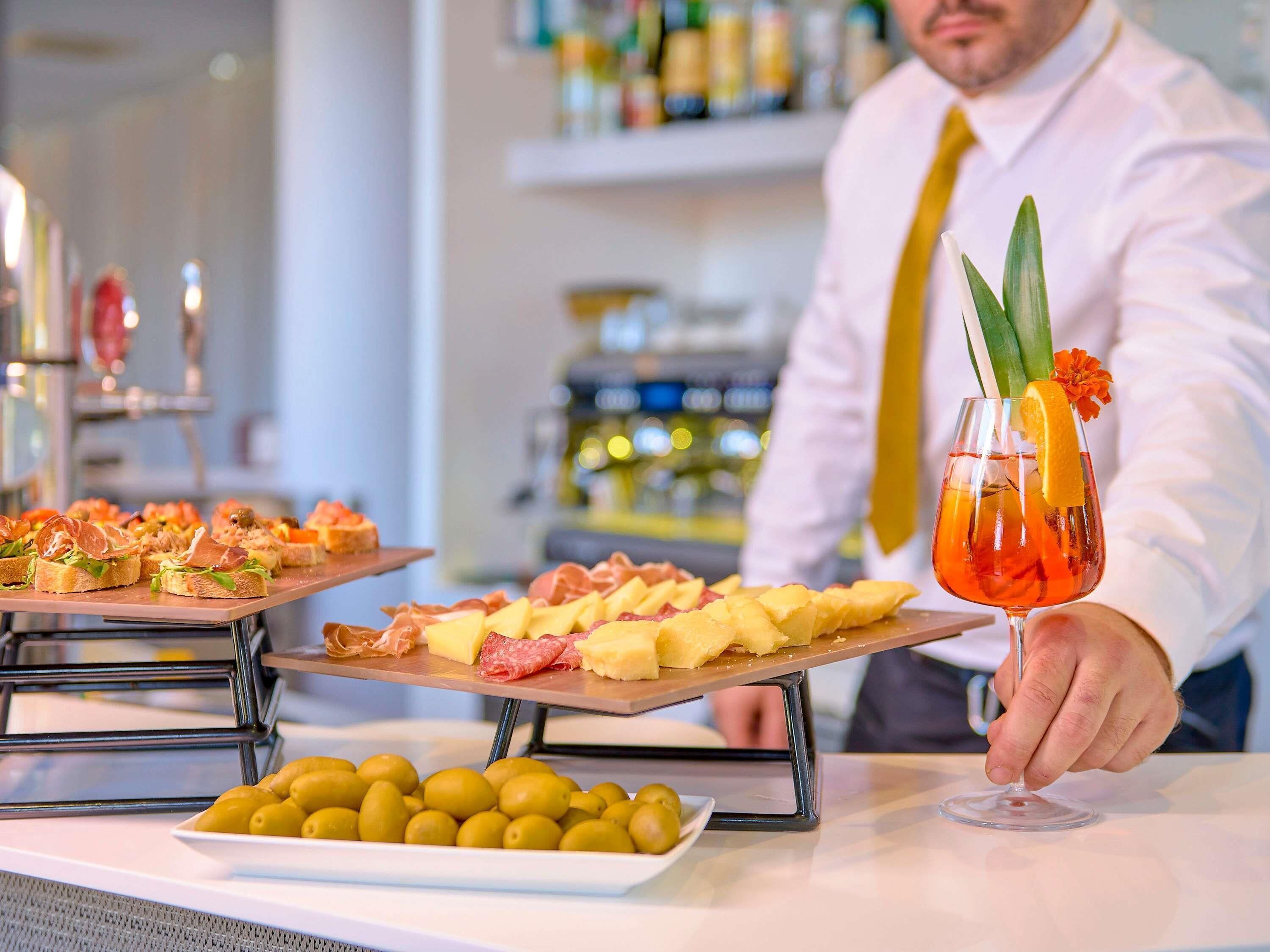 A bar setting with a bartender holding a cocktail, and two platters of appetizers.