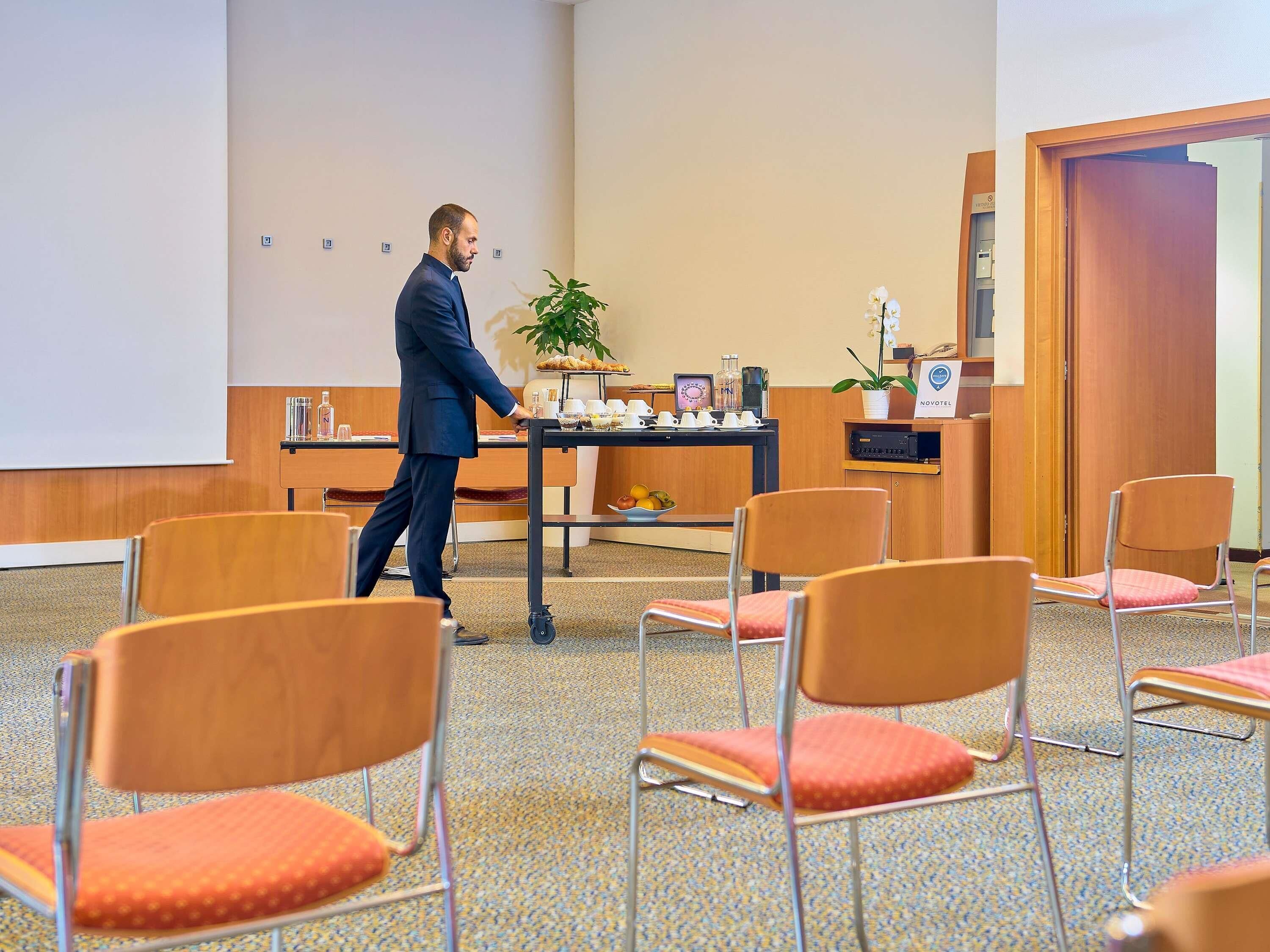 Un salón de conferencias con un atril, sillas, una mesa con una planta y una puerta.