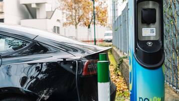 A black car parked next to a blue electric vehicle charging station with a sign that reads 'Charge the Change.'