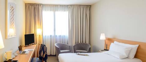 Habitación de hotel con dos camas, un escritorio con computadora, una silla, un televisor y una ventana con cortinas.
