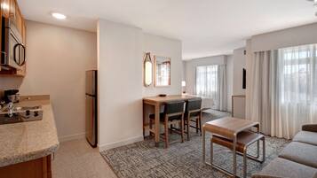 A modern kitchen with a built-in oven, a refrigerator, and a sink. There is a dining area with a table and chairs, and a sofa in the living area.
