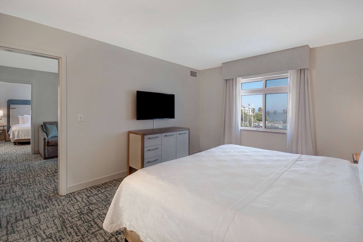 A hotel room with a large bed, a flat-screen TV mounted on the wall, a dresser, and a window with curtains.