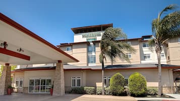 A hotel entrance with a covered walkway, palm trees, and a clear blue sky.