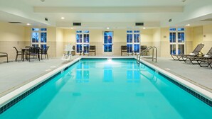 Una amplia piscina interior con agua cristalina y azul, rodeada de tumbonas y una mesa con sillas.