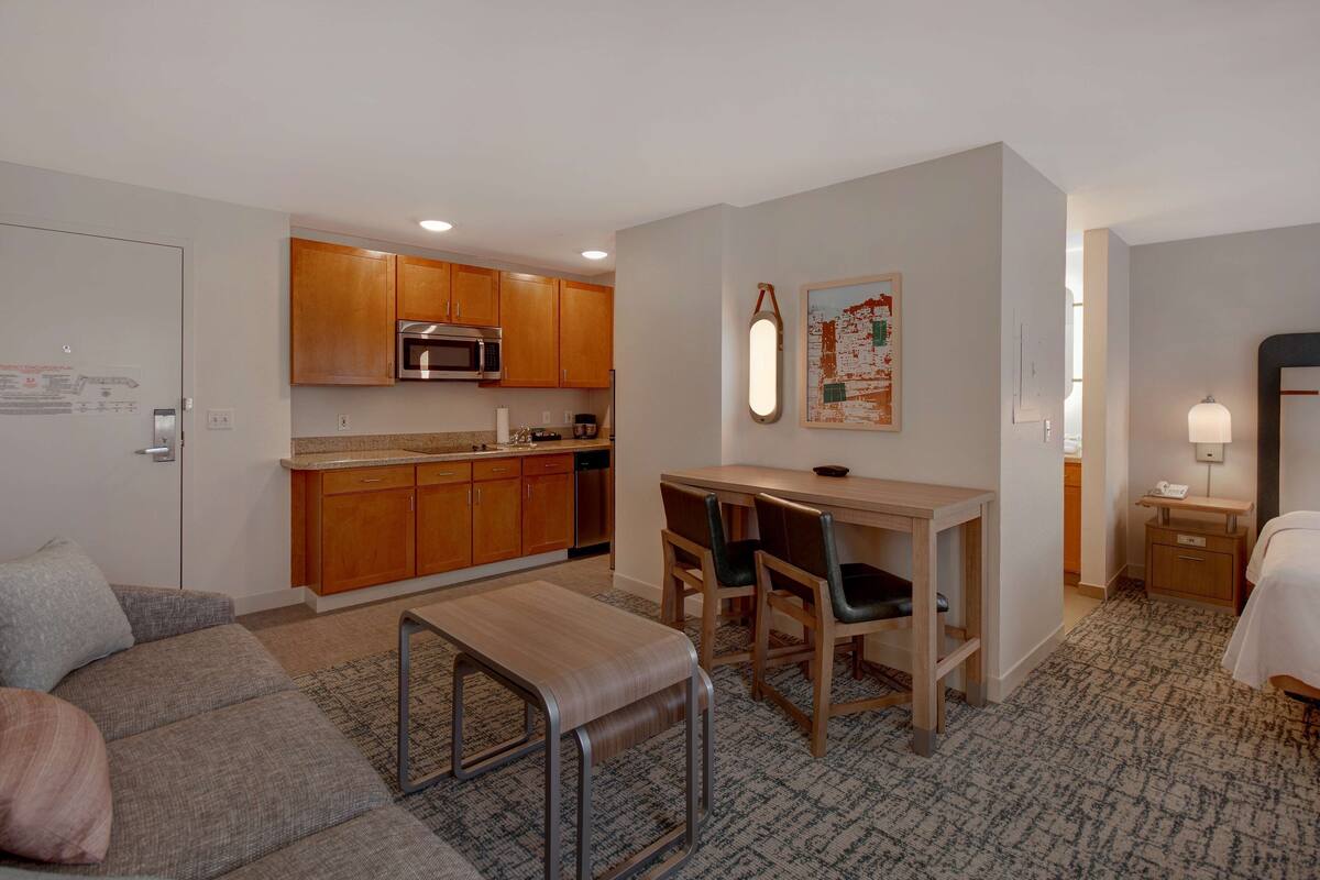 A compact hotel room with a kitchenette, a dining area with a table and chairs, a sofa, and a bed.