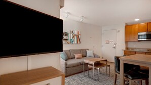 Un espacio habitable compacto con sofá, una mesa de comedor, televisor y zona de cocina.