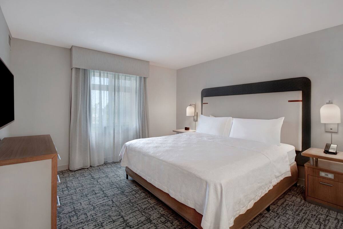 Habitación de hotel con una cama grande, mesitas de noche, un televisor de pantalla plana y una ventana con cortinas.