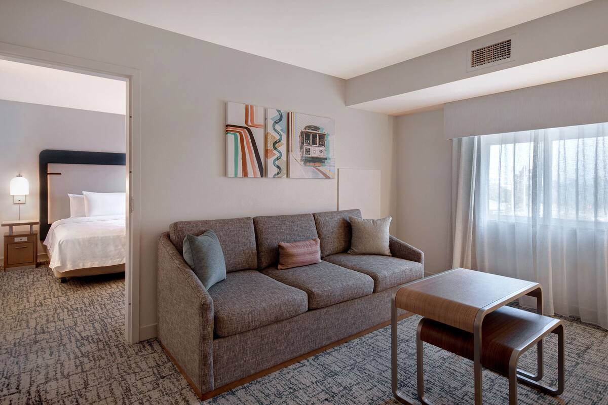 A hotel room with a sofa, a small table, a bed, and a window with curtains.