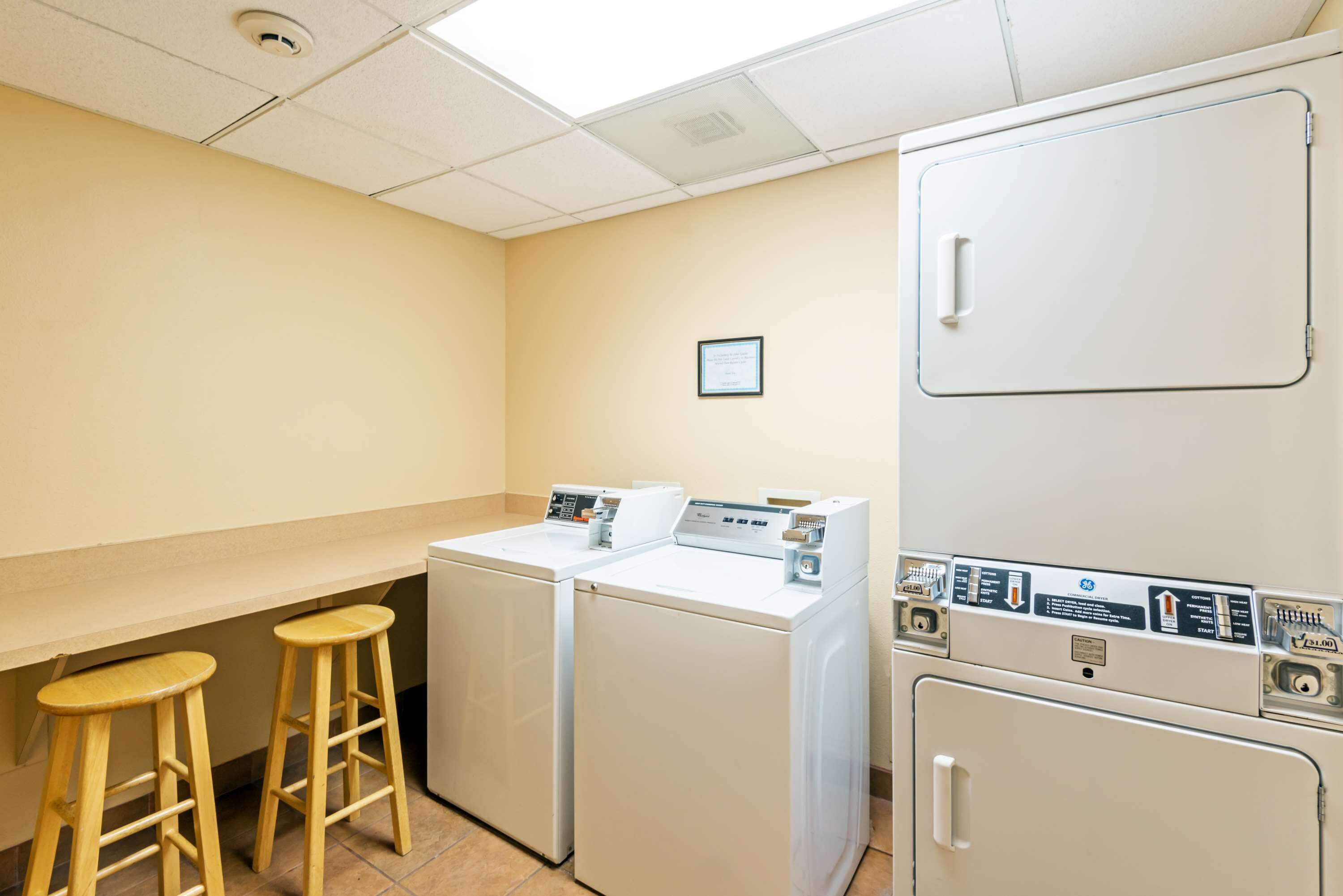 A laundry room with two washing machines, a dryer, and two wooden stools.