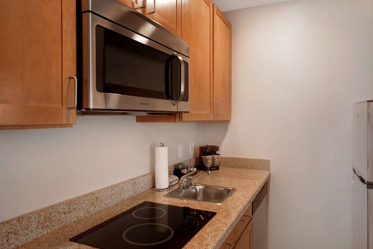 A kitchen with wooden cabinets, a stainless steel microwave, a sink, and a stovetop.