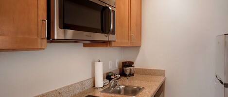 A kitchen with wooden cabinets, a stainless steel microwave, a sink, and a stovetop.