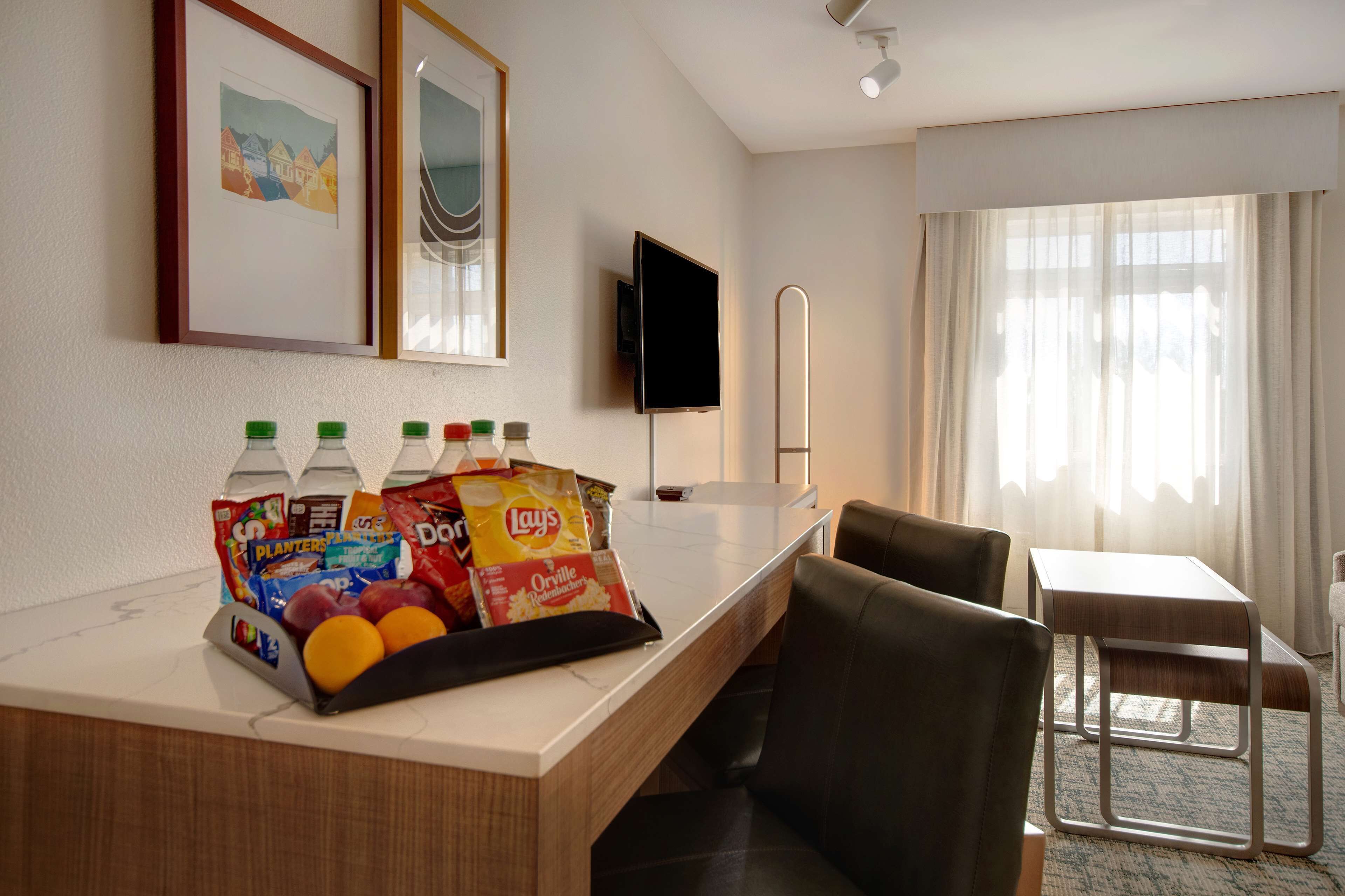 A hotel room with a desk, a flat-screen TV, a chair, and a small table.