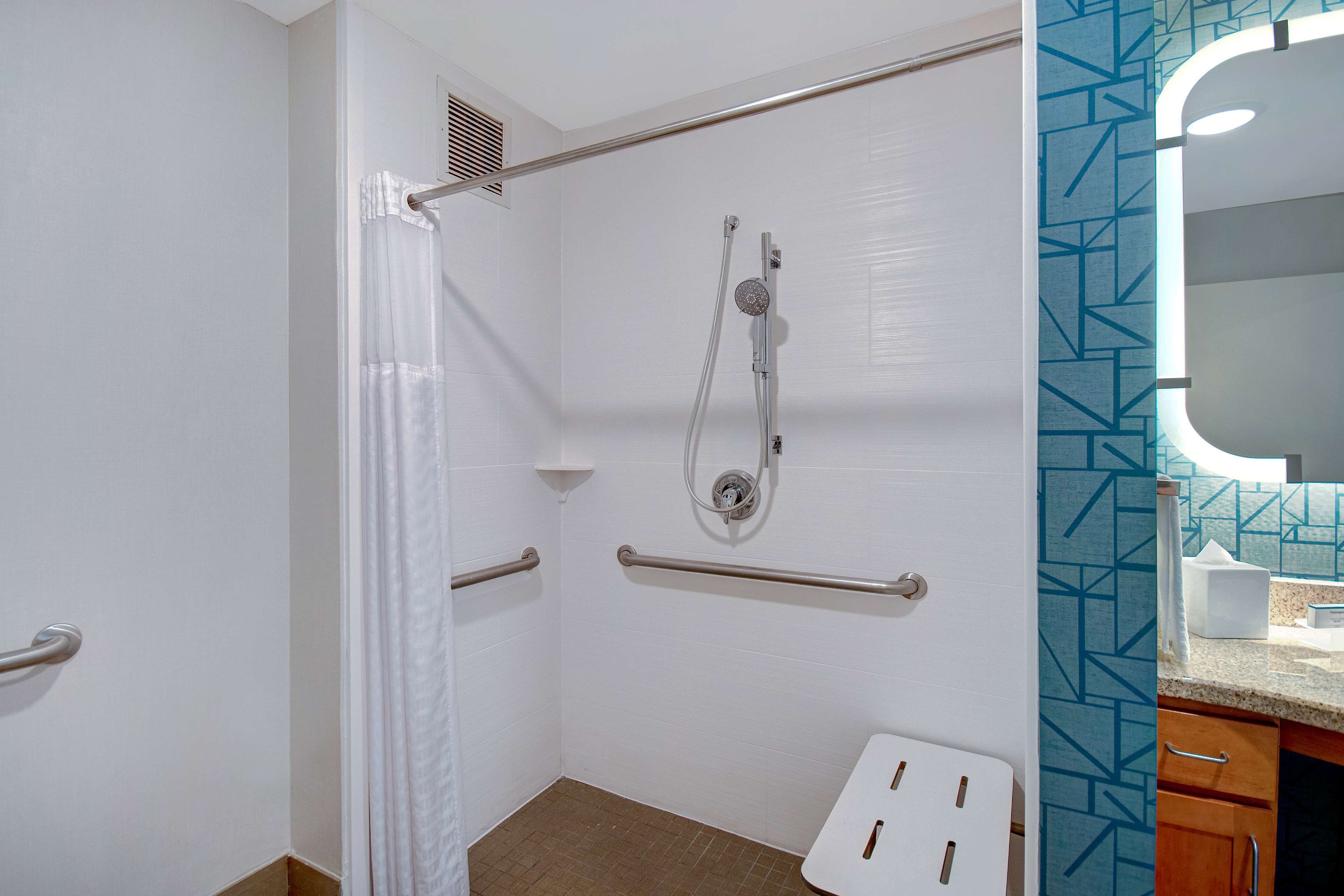 Baño con ducha, barras de apoyo, inodoro y lavabo con espejo.