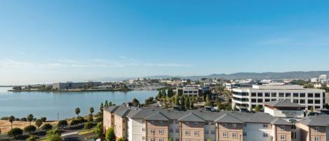 A multi-story hotel with a parking lot in front, a body of water in the background, and a hilly landscape.