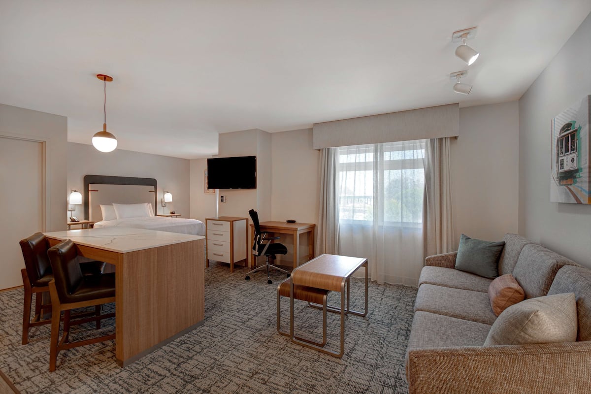 A hotel room with a bed, desk, chair, sofa, and a television.