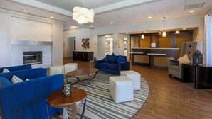 A modern living area with blue sofas, a round table, and a kitchen in the background. - Homewood Suites Southwind - Hacks Cross (Memphis)