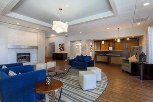 Ein moderner Wohnbereich mit blauen Sofas, einem runden Tisch und einer Küche im Hintergrund.