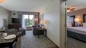 A hotel room with a bed, a TV, a desk with a chair, a sofa, and a dining table set for two. - Homewood Suites Southwind - Hacks Cross (Memphis)