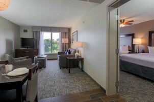 A hotel room with a bed, a TV, a desk with a chair, a sofa, and a dining table set for two.